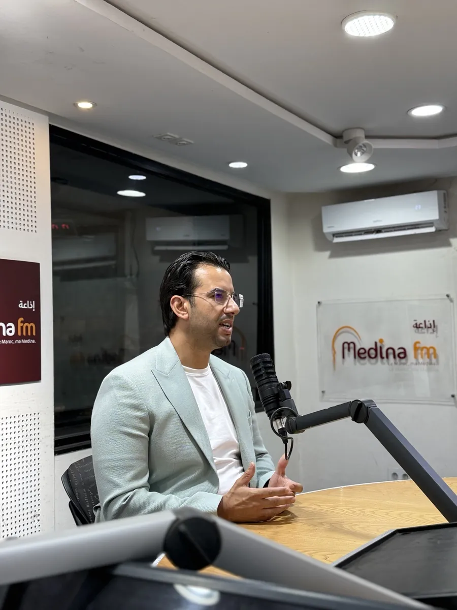 Dr CHARRASS Abdelmajid en veste bleu clair parlant devant un microphone de radio.
