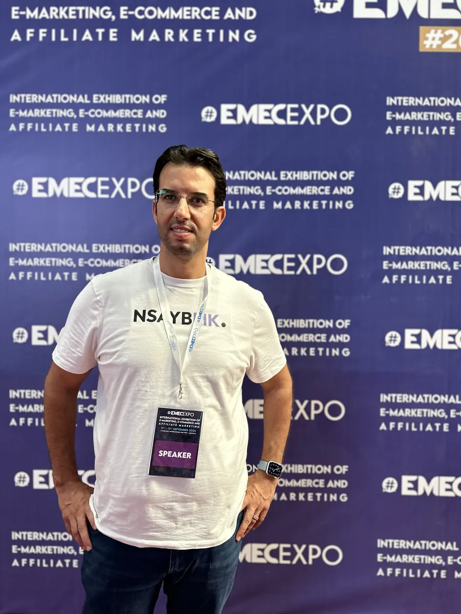 Dr CHARRASS Abdelmajid, badge intervenant, devant le panneau du salon EMEC Expo
