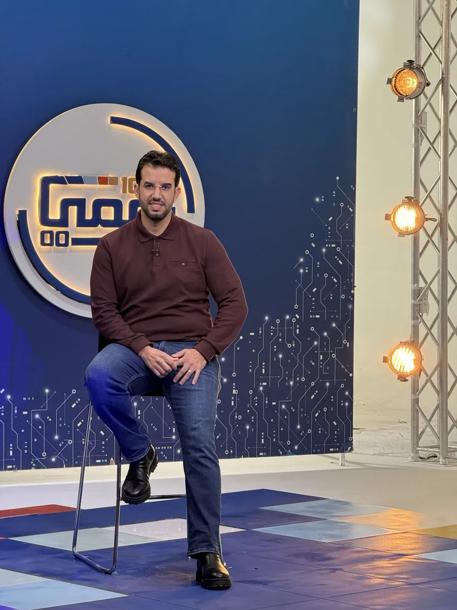 Dr CHARRASS Abdelmajid assis devant un décor bleu, vetu d’un polo bordeaux.